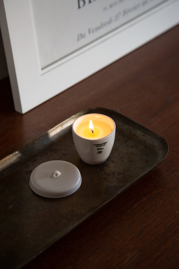 Scientific candle in a ceramic white holder on a dark metal tray with a blurred background