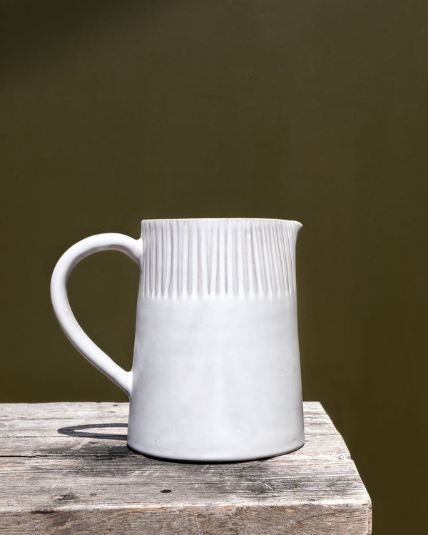 White ceramic pitcher with textured design on a wooden surface against a dark background