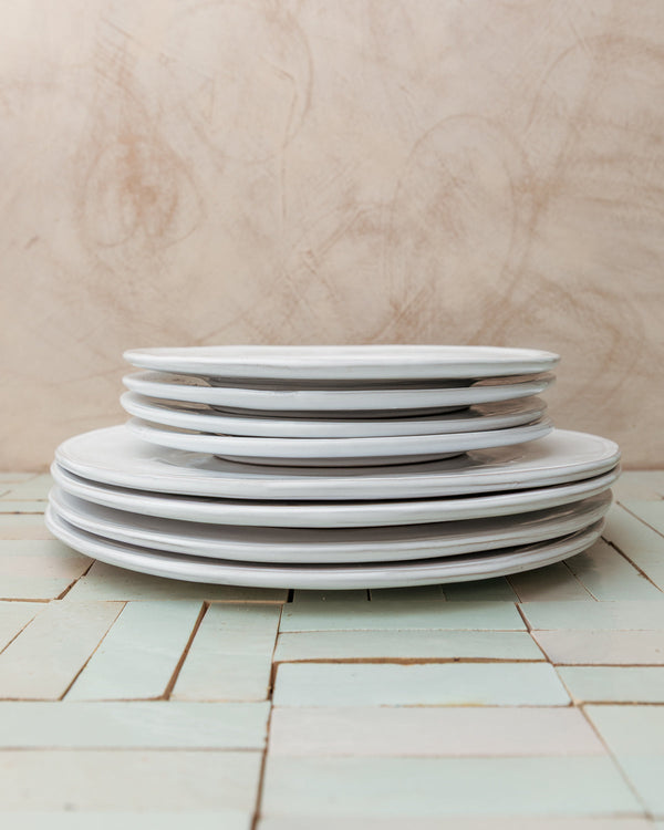 Stack of white ceramic plates on a tiled floor with a wooden wall background