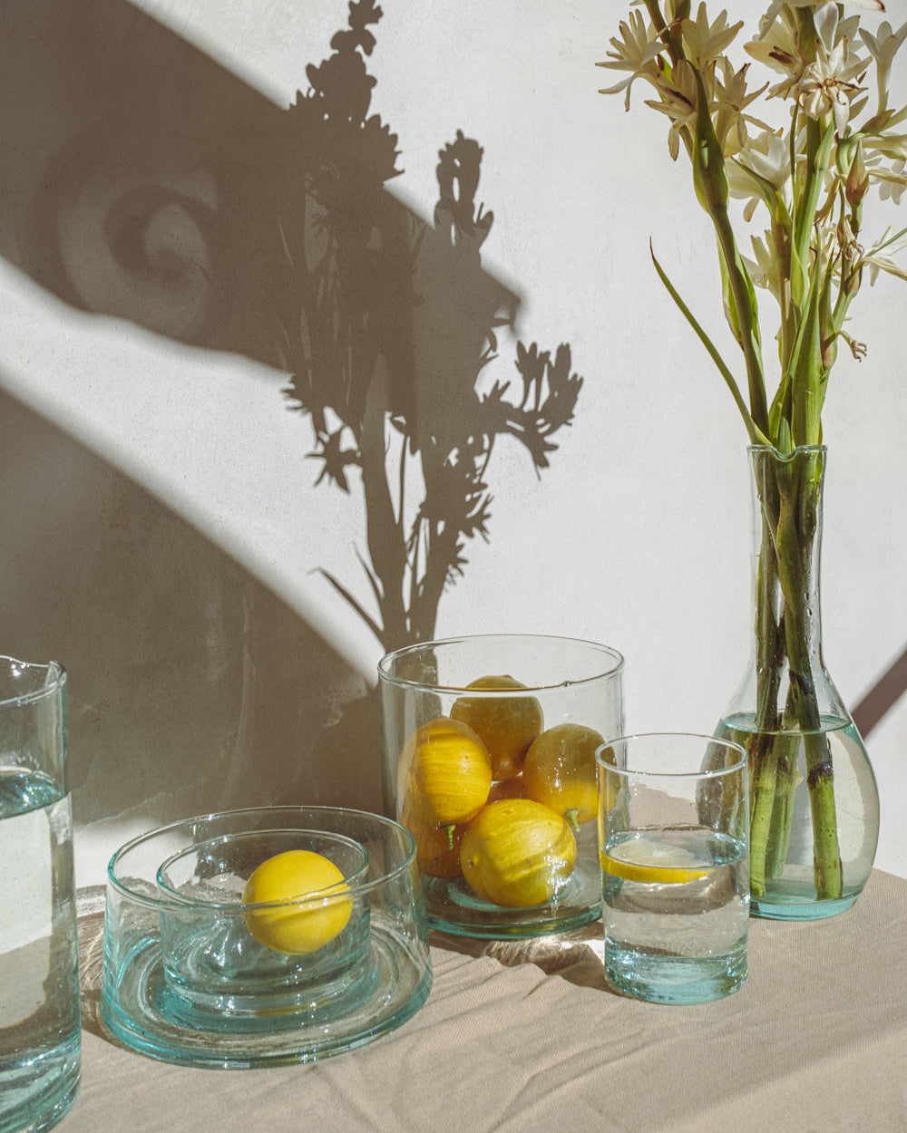 Table setting with lemons, glasses, and a vase with flowers on a neutral background