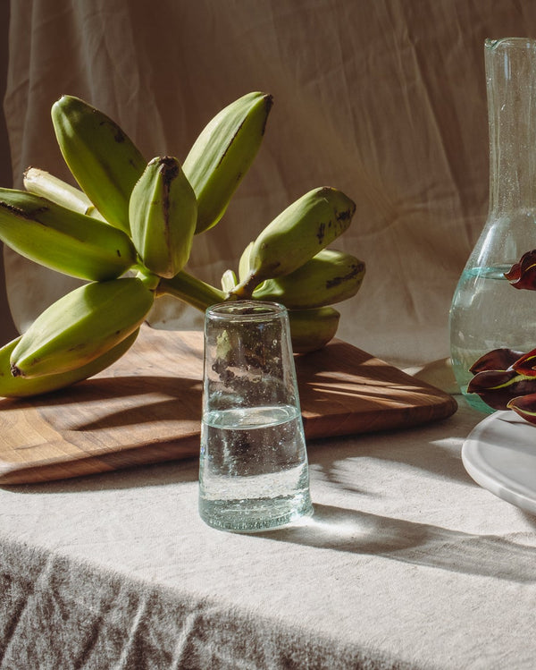 Table setting with bananas, water glasses, and a candle on a textured surface.