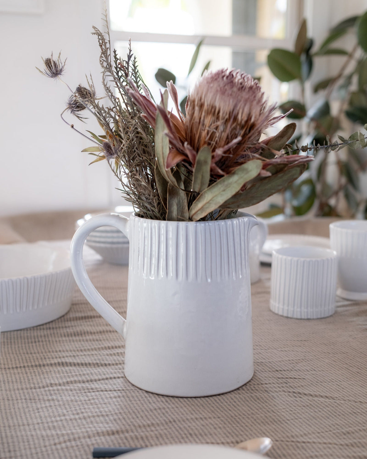White ceramic pitcher with dried flowers on a table