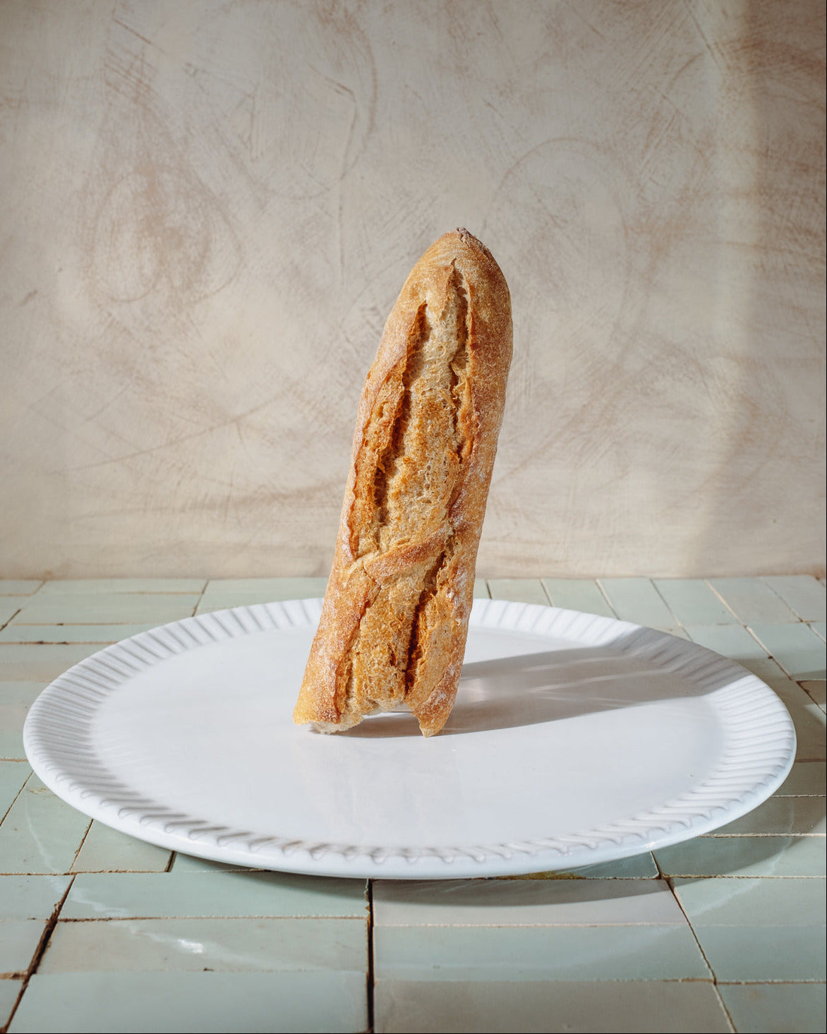 Baguette on a white serving platter with a lime wash background
