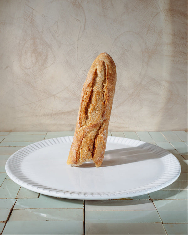 Baguette on a white serving platter with a lime wash background