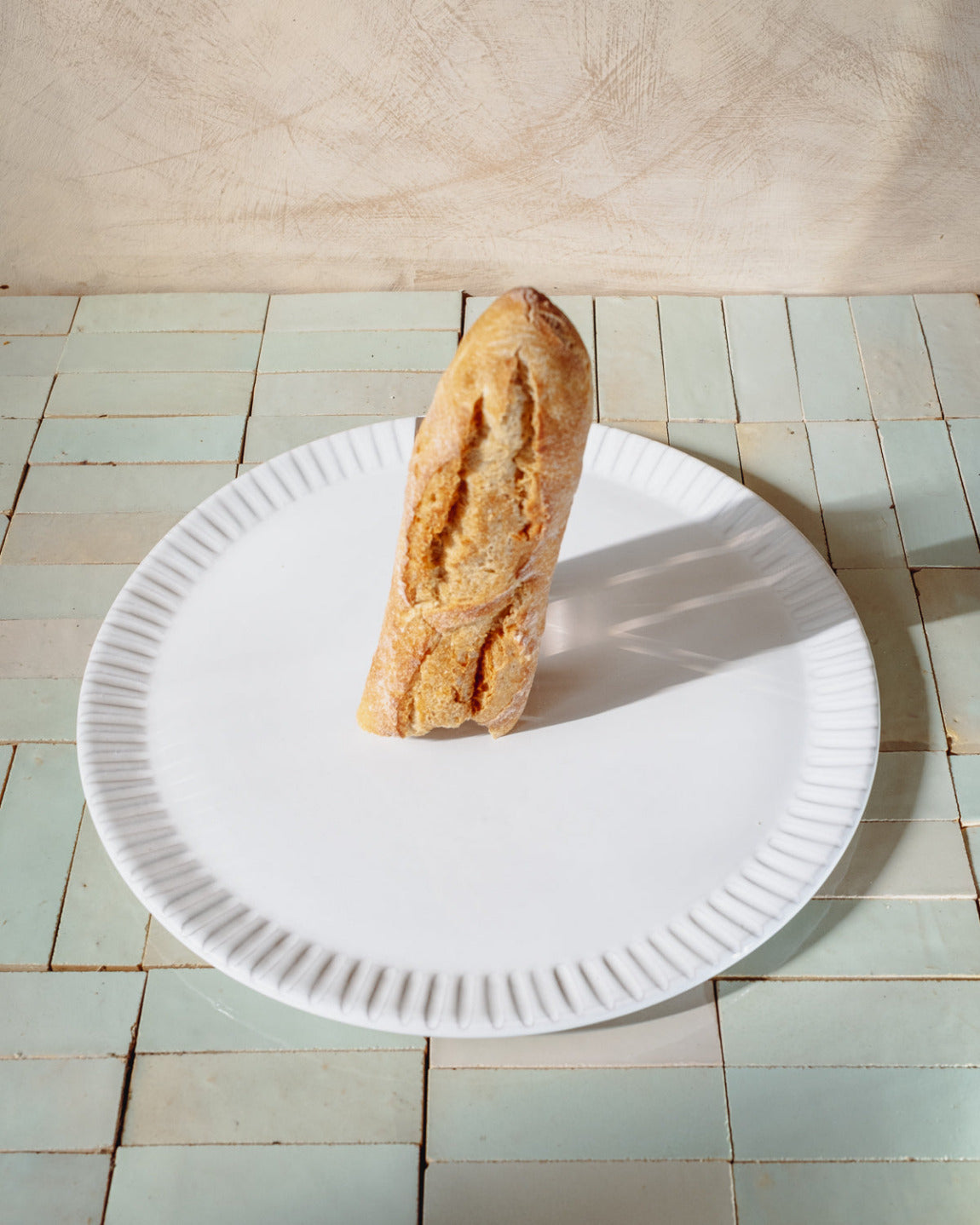 Long loaf of bread on a white paper plate with a tiled floor background